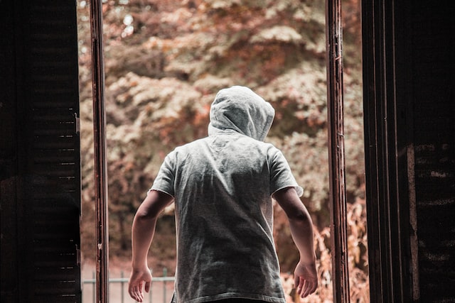 A person wwearing a hoodie tenses and watches out from just outside a dark building